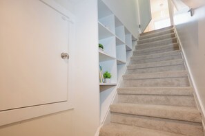 A carpeted staircase with a white door on the left and a white wall with shelves on the right. - Cottage with Sauna, Fenced Backyard, Near Stadiums (Seattle)