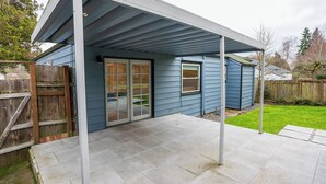 Un patio couvert, doté d’une porte-fenêtre coulissante et d’une fenêtre, est entouré d’une clôture en bois et d’une pelouse.