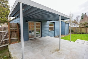 A covered patio area with a sliding glass door and a window, surrounded by a wooden fence and a grassy yard.