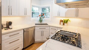 Une cuisine moderne avec des meubles blancs, un lave-vaisselle encastré, une cuisinière à gaz et une fenêtre donnant sur un paysage verdoyant.