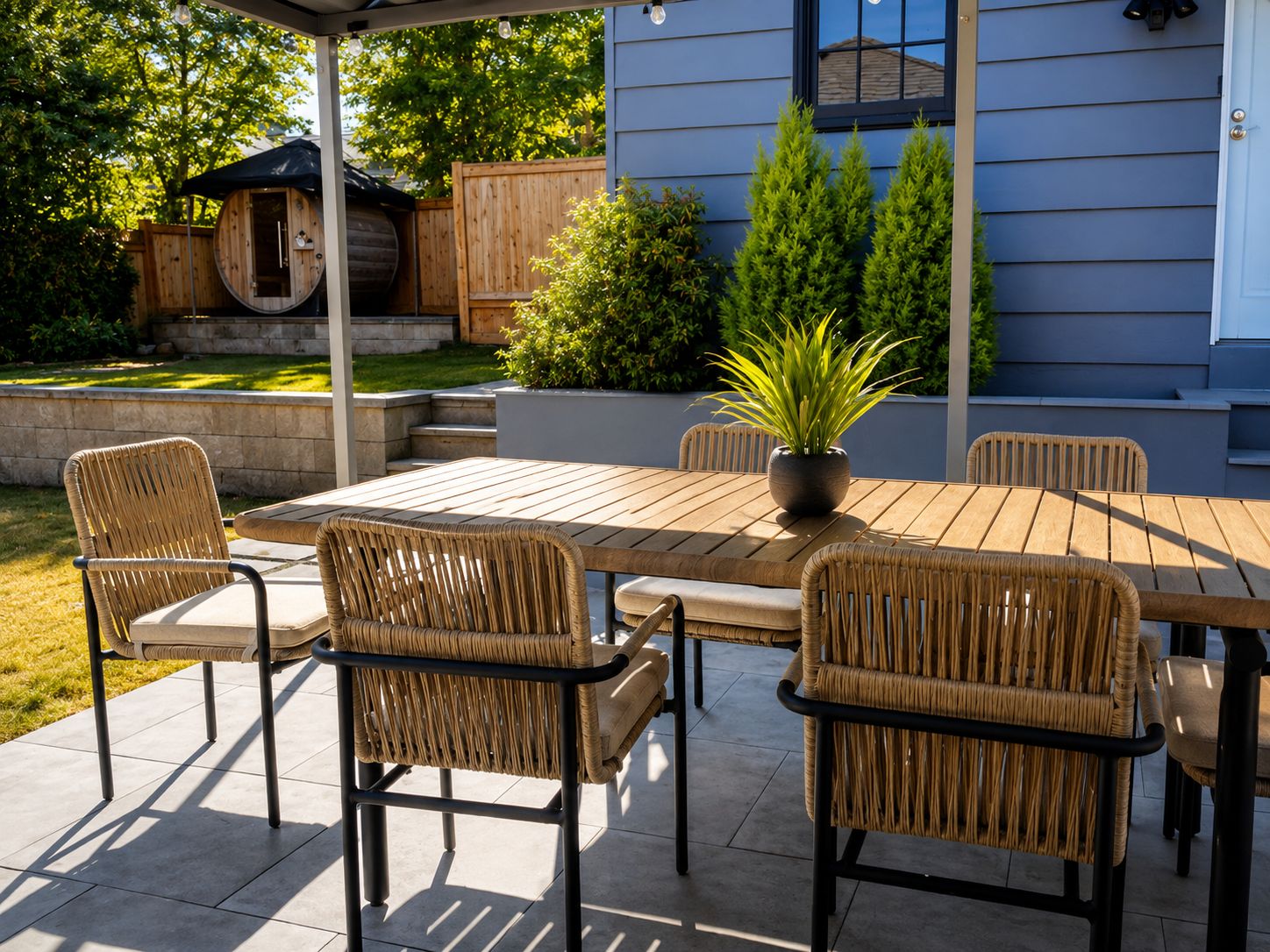 An outdoor patio with a table and chairs, a potted plant, and a wooden fence.