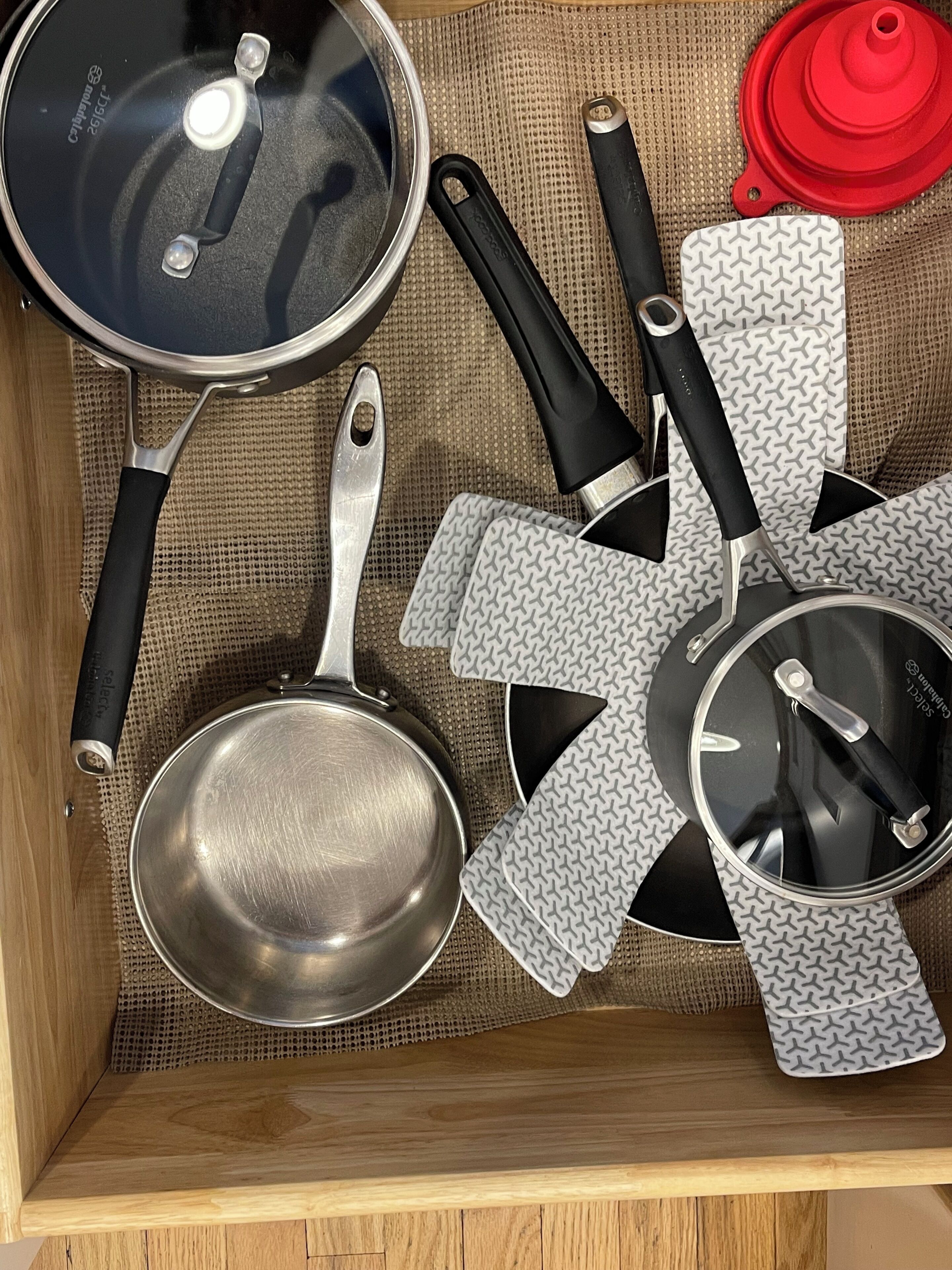 A drawer containing various kitchen utensils including a frying pan, spatulas, and a pot lid.