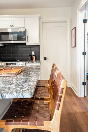 A kitchen with white cabinets, a black tiled backsplash, a wooden bench with a woven seat, and a marble countertop. - CUSTOM FALCON PUTTING GREEN and Luxury combined to create your DREAM stay here in the heart of Bowling Green! (Bowling Green)