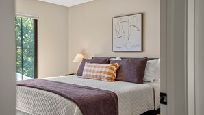 Ein Schlafzimmer mit Bett, Fenster, Wandlampe und einem abstrakten Kunstwerk.
