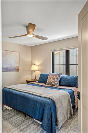 Ein Schlafzimmer mit einem Bett, einem Deckenventilator, einem Fenster und einem Bild an der Wand.
