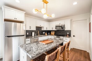 A modern kitchen with white cabinets, a stainless steel refrigerator, a granite island, and a pendant light fixture. - CUSTOM FALCON PUTTING GREEN and Luxury combined to create your DREAM stay here in the heart of Bowling Green! (Bowling Green)