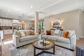 A modern living room with two grey sofas, a coffee table, and a kitchen in the background. - CUSTOM FALCON PUTTING GREEN and Luxury combined to create your DREAM stay here in the heart of Bowling Green! (Bowling Green)
