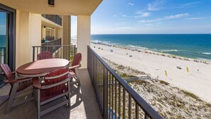 A balcony with a table and chairs, overlooking a beach with umbrellas and people. - Phoenix Iv 4082 1 Bedroom Condo (Orange Beach)