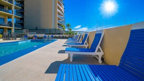 Zona junto a la piscina con sillas reclinables azules, una piscina y un edificio alto con balcones.