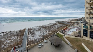 Blick auf einen Strand mit einer Pier, einem Poolbereich und einem Gebäude mit Balkonen.