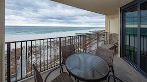 A balcony with a glass table and wicker chairs, overlooking a beach with a pier. - Phoenix Iv 4042 1 Bedroom Condo (Orange Beach)