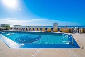 Ein Swimmingpool mit Sonnensegel und Rettungsschwimmerstand sowie freiem Blick auf den Ozean.