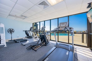 A gym with treadmills, elliptical machines, and a fan, overlooking a pool. - Phoenix Iv 4122 1 Bedroom Condo (Orange Beach)
