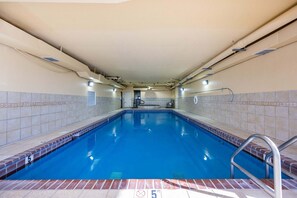 Una piscina interior con superficie de agua cristalina, paredes de azulejos y una escalera metálica de acceso.