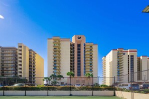 Un immeuble résidentiel de grande hauteur, doté de nombreux balcons, d’une entrée principale et surplombant un ciel d’un bleu éclatant.