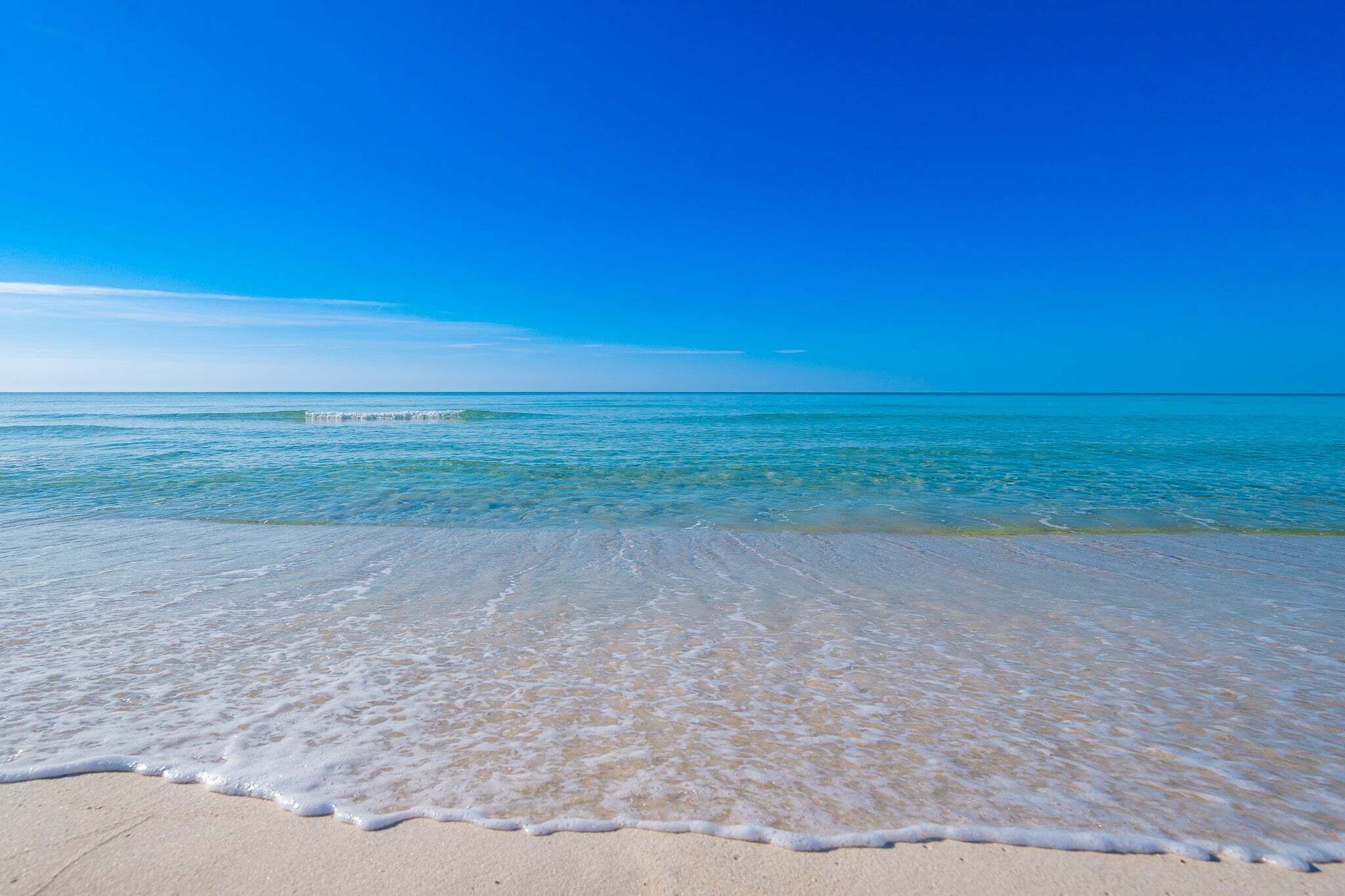 A beach with clear blue water and a sandy shore.