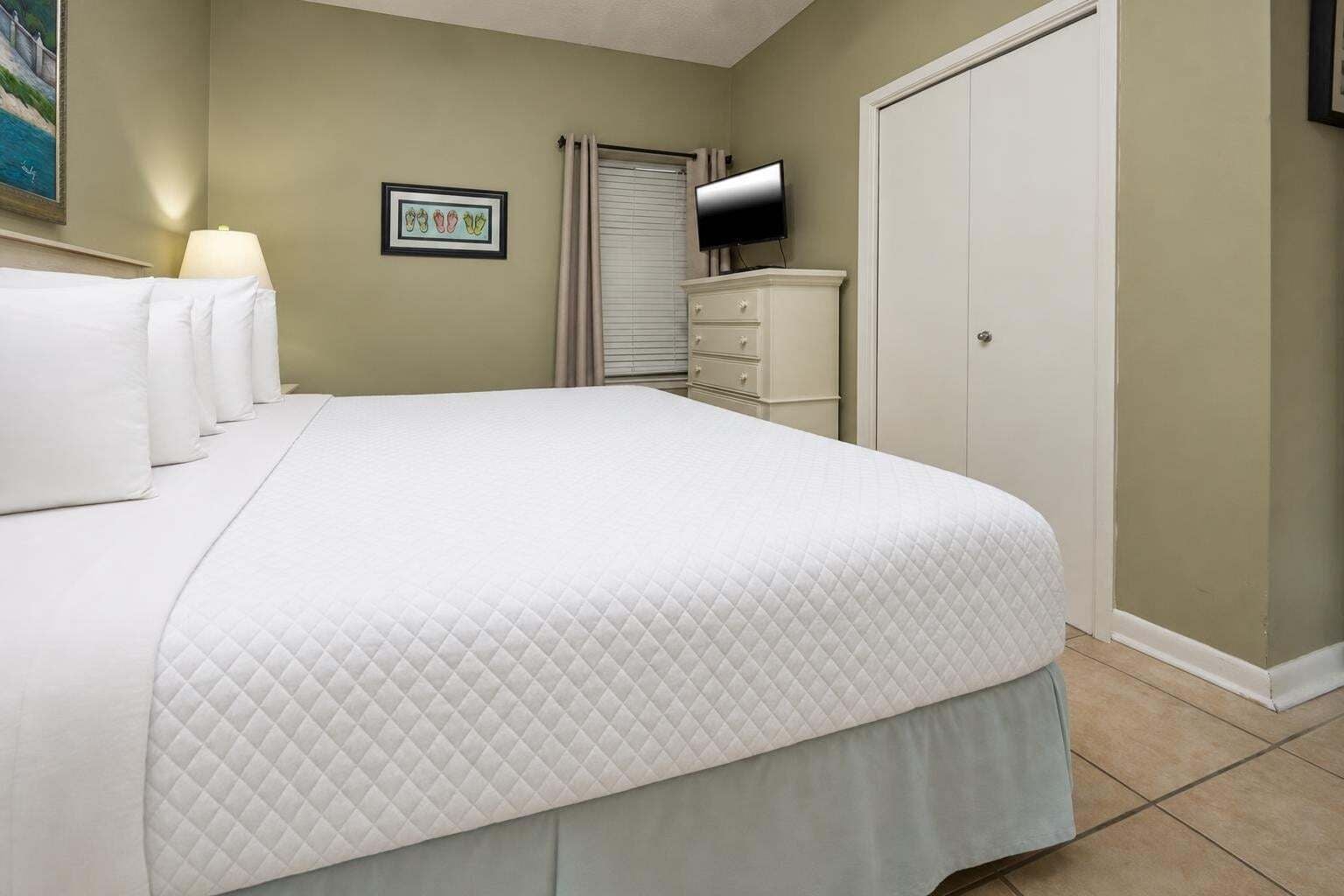 A bedroom with a large bed, a dresser, a television, and a door.