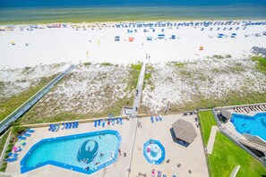 Een strandresort met een groot zwembadgedeelte, strandparasols en een zandstrand.
