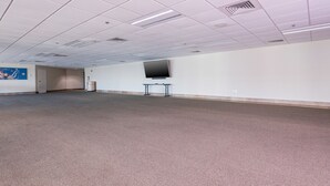 A large, empty room with a carpeted floor, white walls, and a flat-screen TV mounted on the wall. - Phoenix Ix 1202 2 Bedroom Condo (Orange Beach)