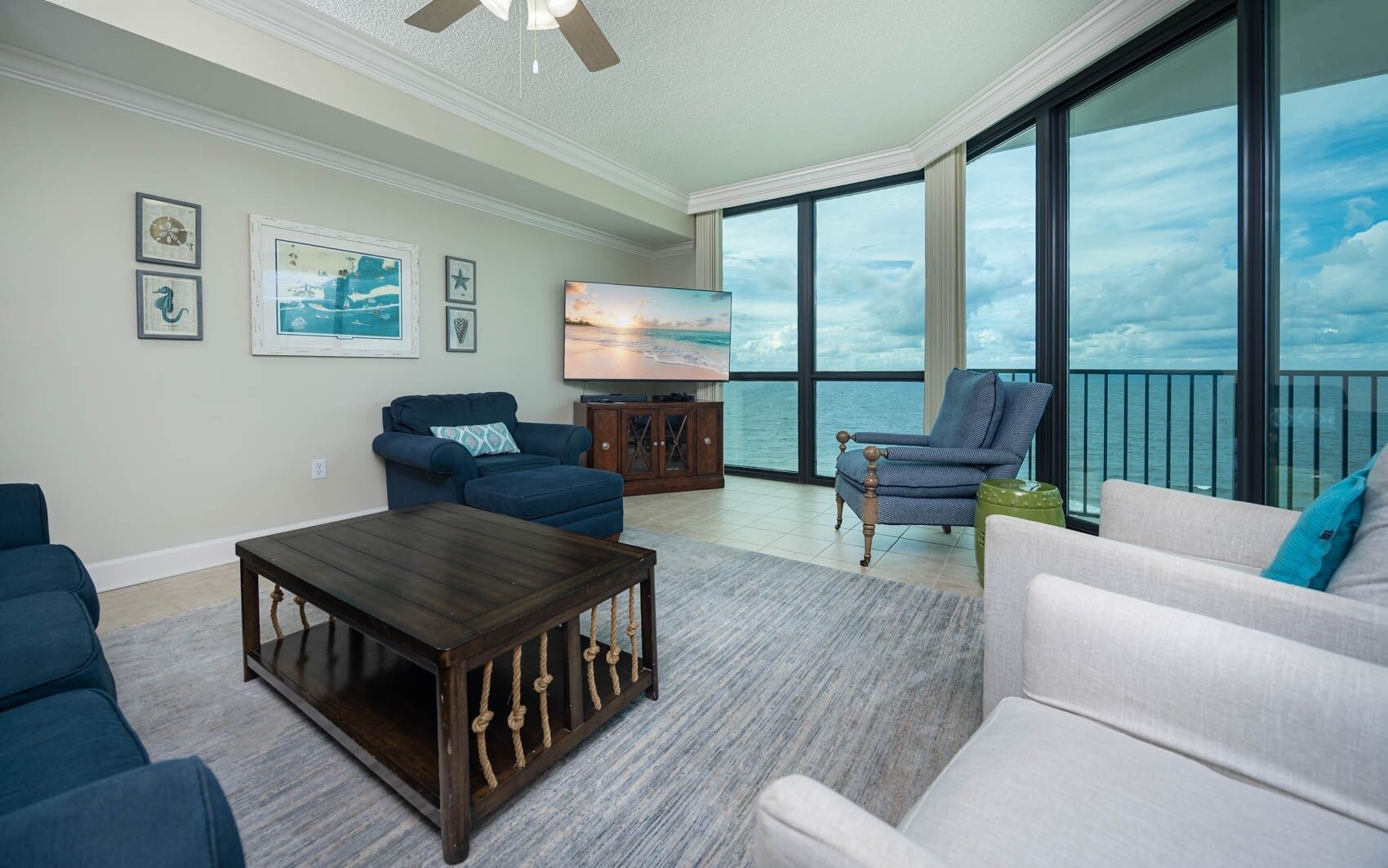 A spacious living room with a large window overlooking the ocean, a television, and comfortable seating.
