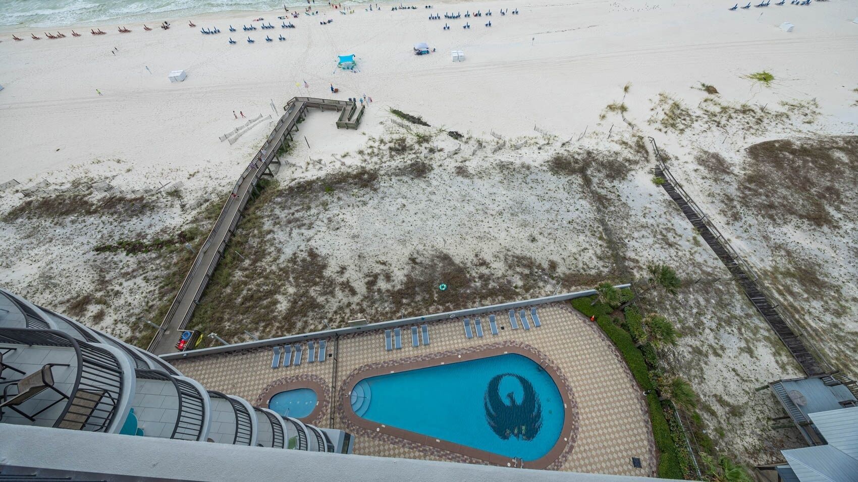 Uitzicht op het strand vanaf een hoger punt, inclusief een zwembad met een uniek ontwerp, een pier en een zandstrand met parasols.