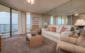 A spacious living room with a large window, a sofa, a chair, and a coffee table. - Phoenix Iv 4104 2 Bedroom Condo (Orange Beach)