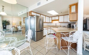 Una cocina moderna con una isla central, sillas de mimbre blancas y una mesa de comedor de vidrio.