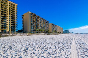 A beachfront hotel with multiple high-rise buildings, sandy beach, and clear blue sky. - Phoenix Iv 4062 1 Bedroom Condo (Orange Beach)