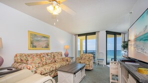 A living room with a sofa, coffee table, and chairs, a painting on the wall, and a balcony with a view. - Phoenix Iv 4062 1 Bedroom Condo (Orange Beach)