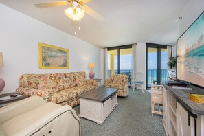 A living room with a sofa, coffee table, and chairs, a painting on the wall, and a balcony with a view. - Phoenix Iv 4062 1 Bedroom Condo (Orange Beach)