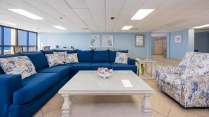A room with a blue sofa, a white coffee table, and a floral armchair. There are framed pictures on the wall, and a door in the background. - Phoenix Iv 4022 1 Bedroom Condo (Orange Beach)