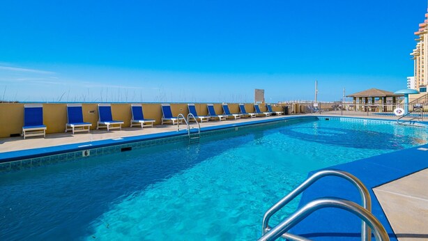 A swimming pool with lounge chairs, a lifeguard stand, and a building in the background. - Phoenix Iv 4022 1 Bedroom Condo (Orange Beach)