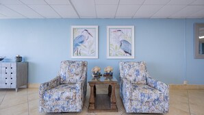 A room with two floral-patterned armchairs, a wooden table with decorative items, and framed bird paintings on the wall. - Phoenix Iv 4022 1 Bedroom Condo (Orange Beach)