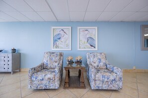 A room with two floral-patterned armchairs, a wooden table with decorative items, and framed bird paintings on the wall. - Phoenix Iv 4022 1 Bedroom Condo (Orange Beach)