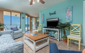 A living room with a TV, a coffee table, and a sofa. There is a chair and a plant. The room has a view of the sea. - Phoenix Iv 4022 1 Bedroom Condo (Orange Beach)