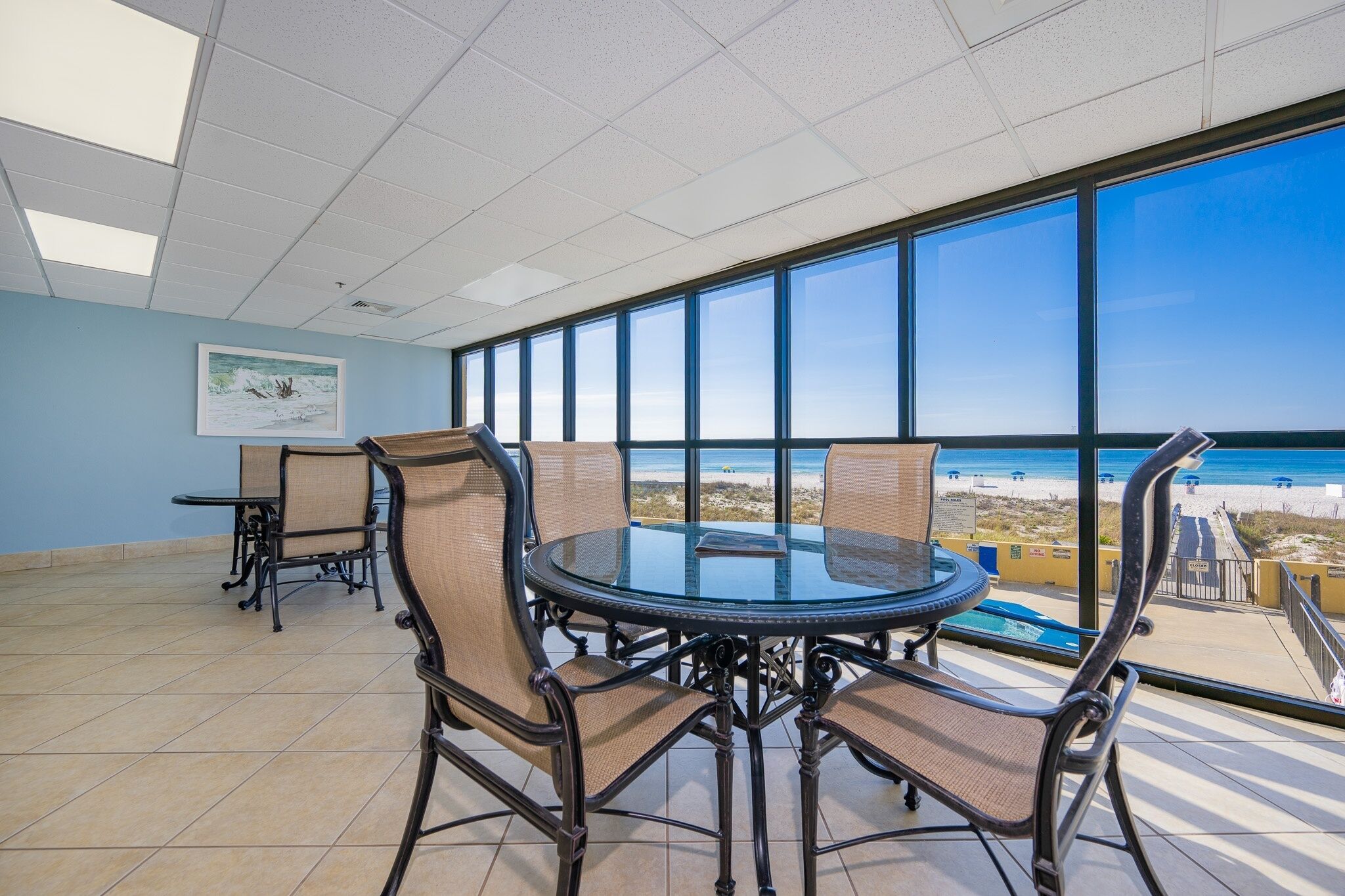 Un salón de conferencias con una mesa y sillas de vidrio, ventanas amplias con vista a la playa y suelo de baldosas.