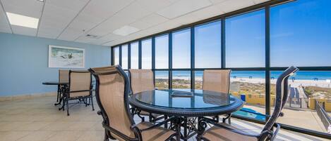 Un salón de conferencias con una mesa y sillas de vidrio, ventanas amplias con vista a la playa y suelo de baldosas.