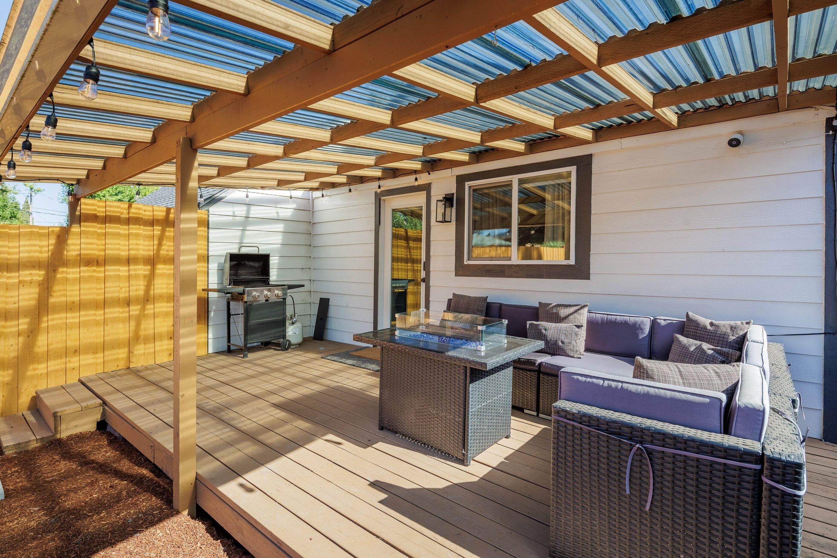 Un patio techado con una parrilla, mobiliario exterior y una estructura de pérgola.