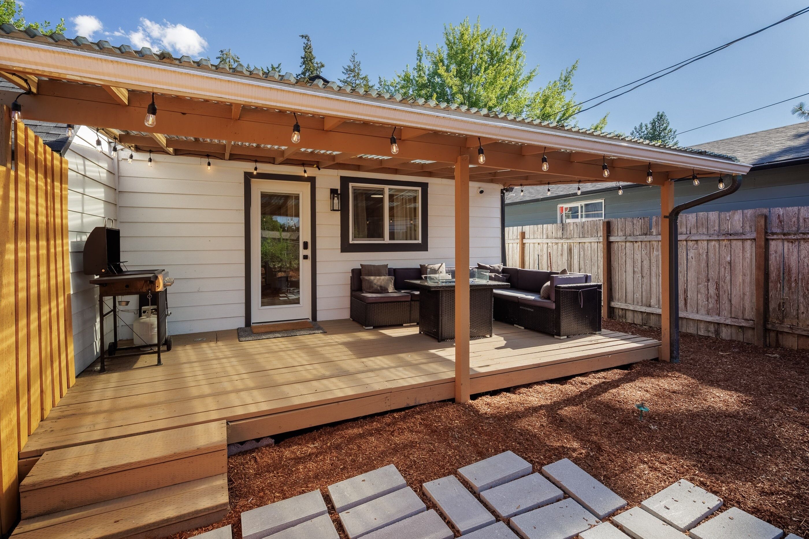 A covered patio with outdoor furniture, a grill, and a pergola with string lights.