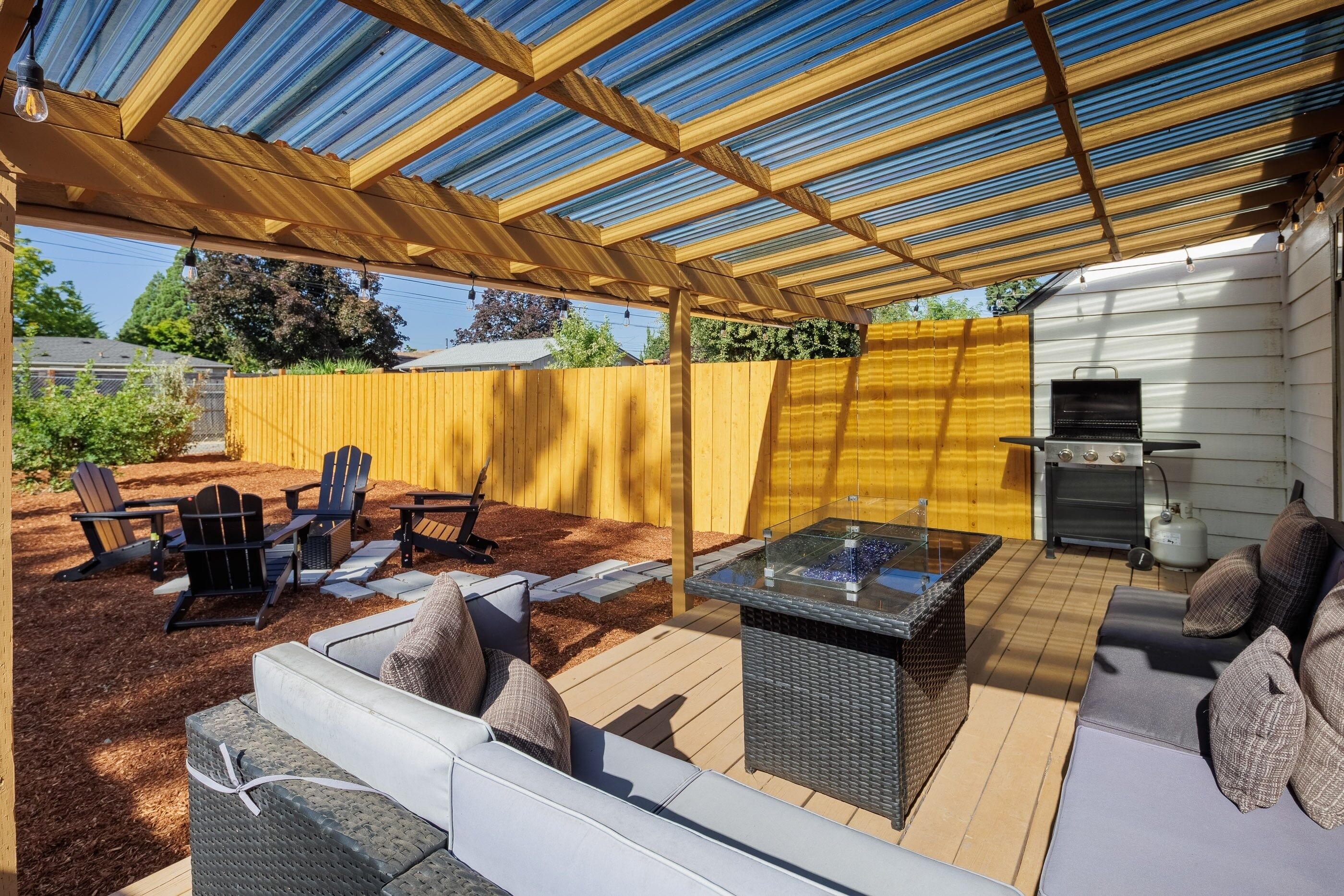 A covered patio with a grill, outdoor seating, and a pergola structure.