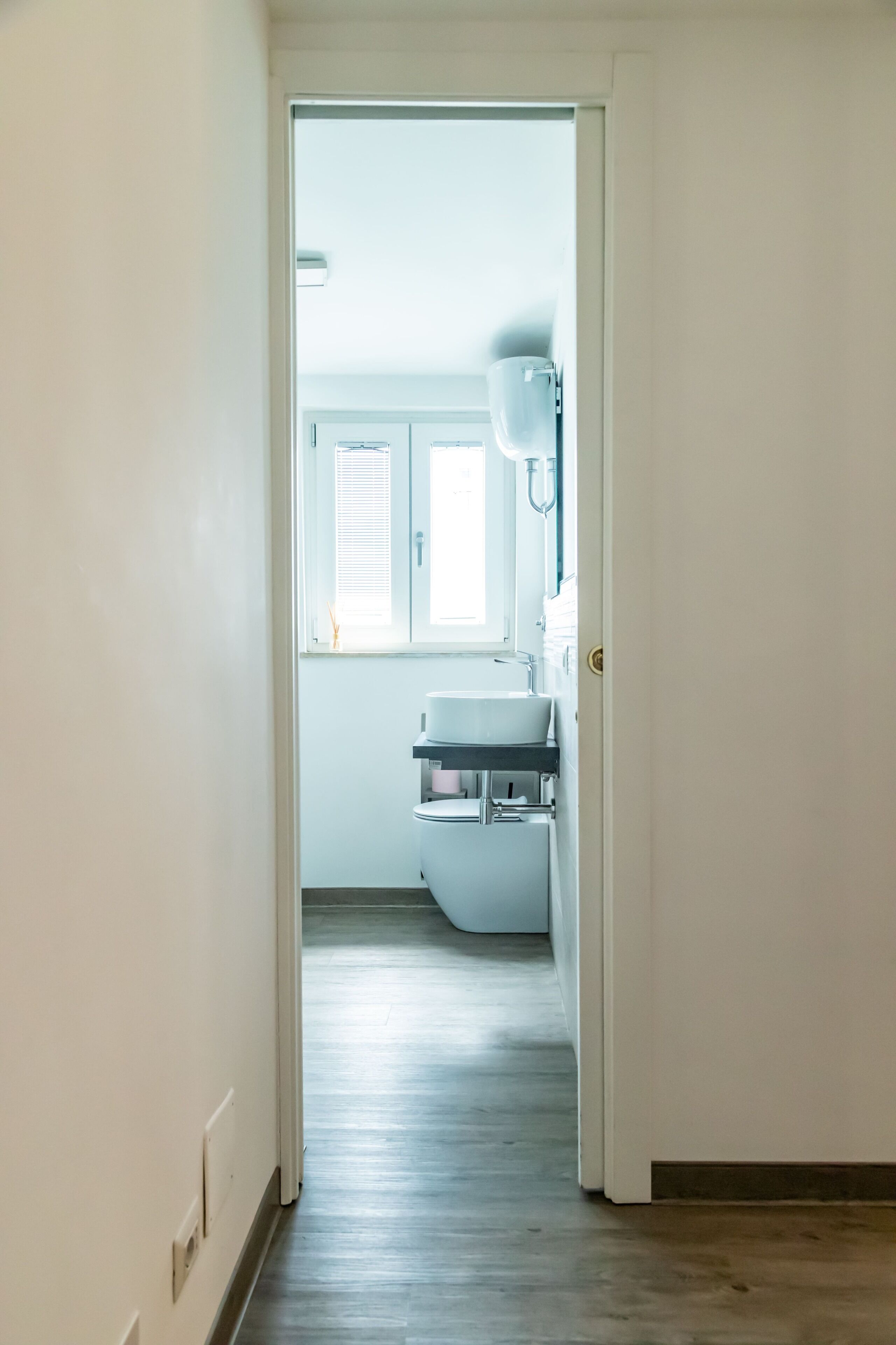 A narrow hallway leading to a bathroom with a toilet, sink, and window.