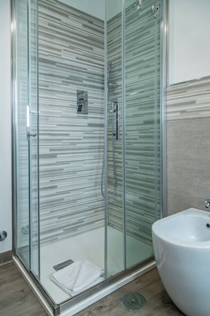 A modern bathroom with a glass-enclosed shower, a white sink, and a striped tile wall. - Circo Massimo Room  (Roma)