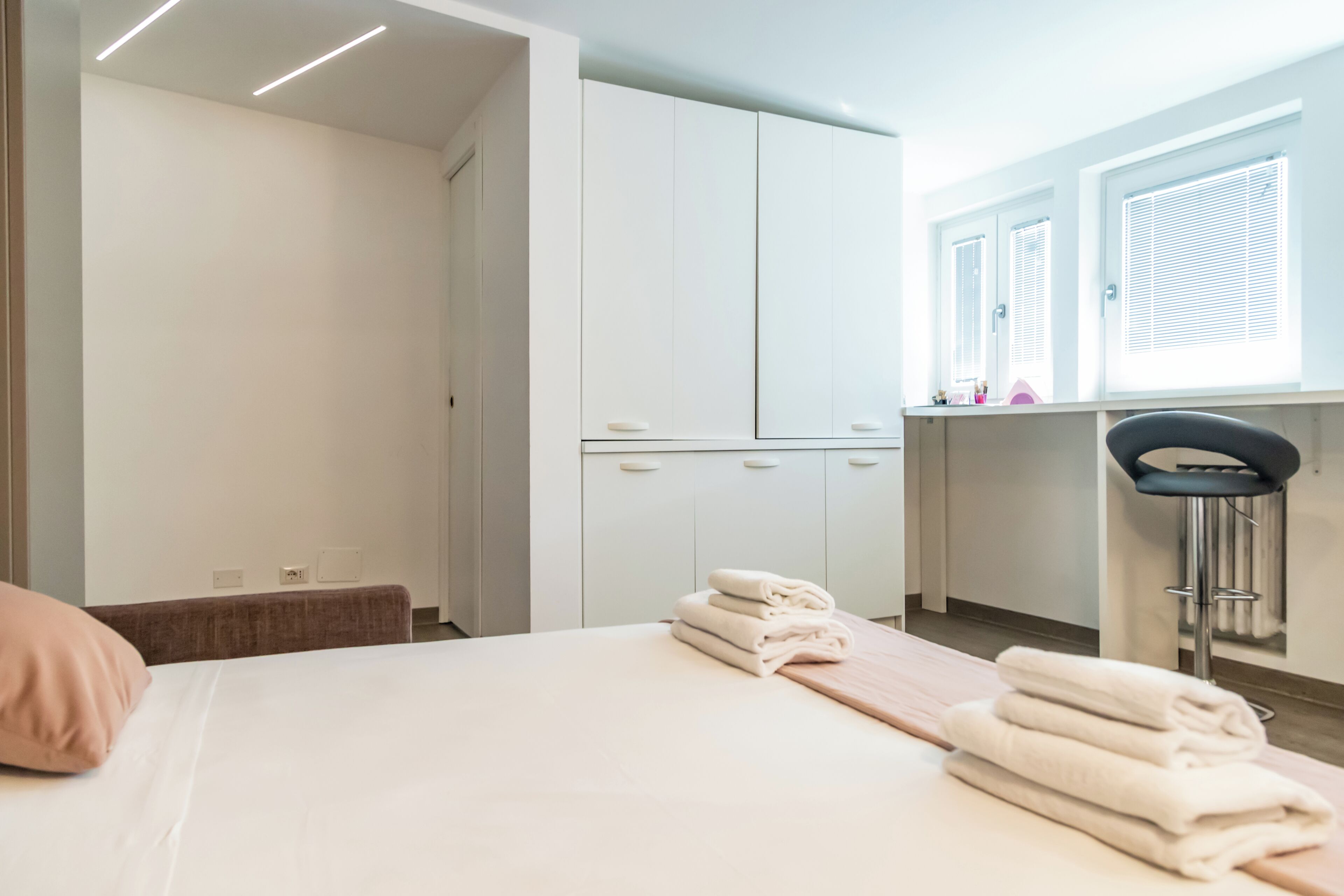 A hotel room with a bed, a chair, a desk, and a window with blinds.