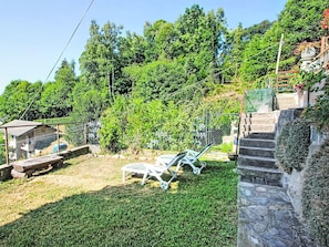 Ein Garten mit Rasen, einer Holzterrasse und einer Steintreppe, die zu einer höheren Ebene führt.