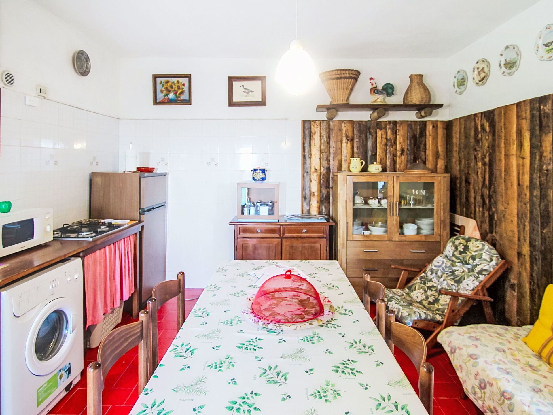 Eine kompakte Küche mit Essbereich, einer Waschmaschine, einer Mikrowelle und einem Tisch mit Blumenmuster-Tischdecke.