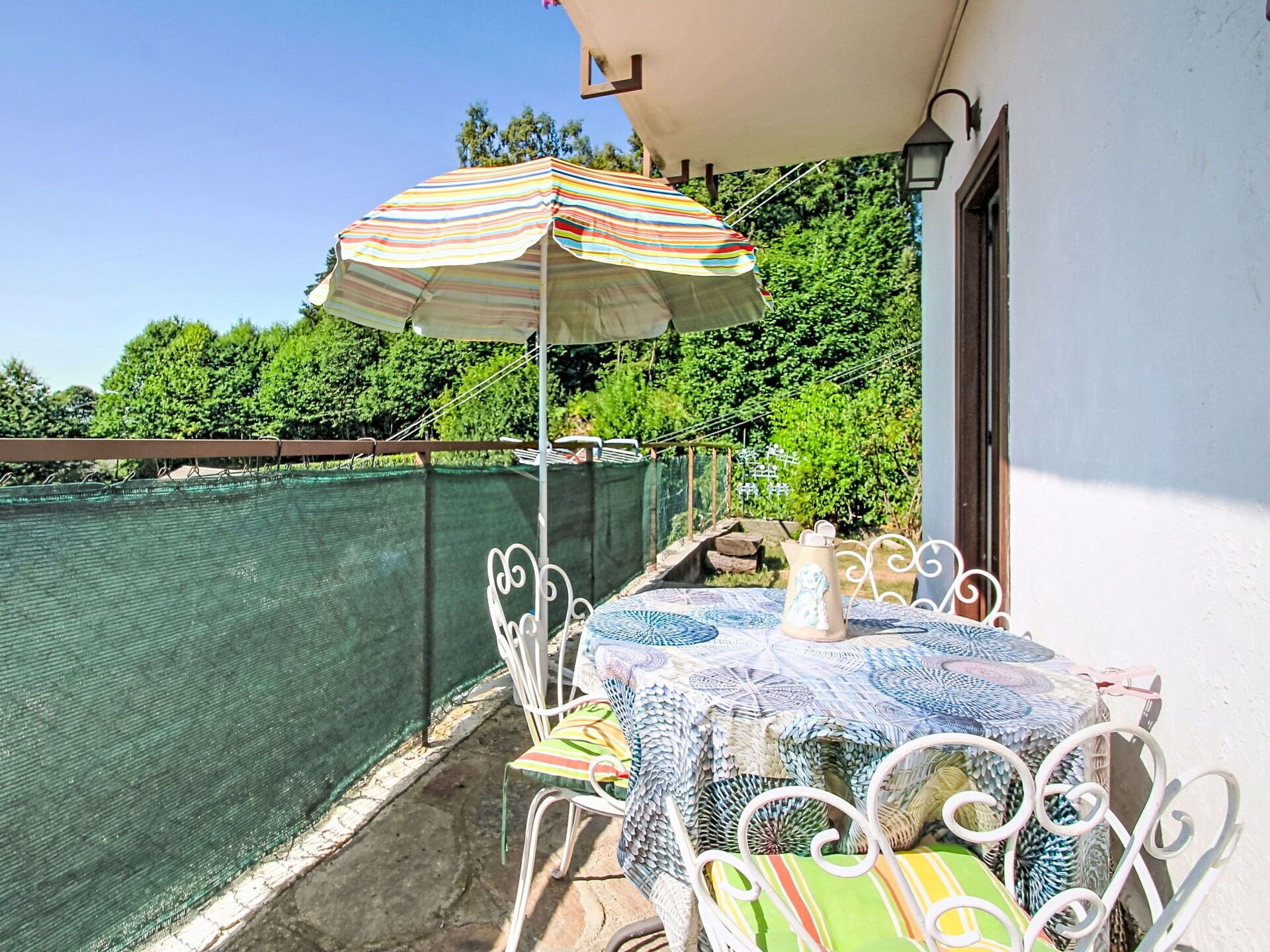 Ein Balkon mit Tisch und Stühlen, einem Streifen-Sonnenschirm und einem Pool.