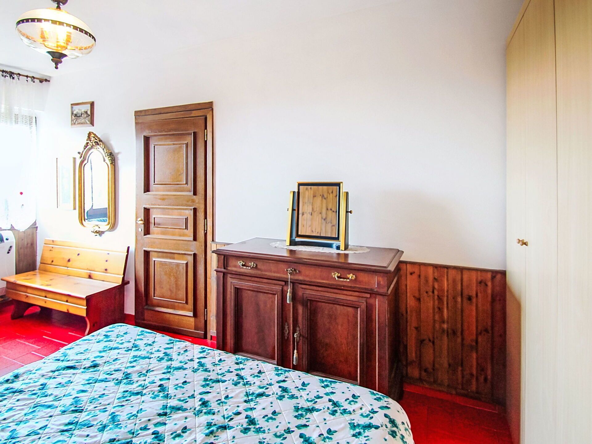 Une chambre à coucher avec un lit, une armoire en bois, un banc et un miroir.