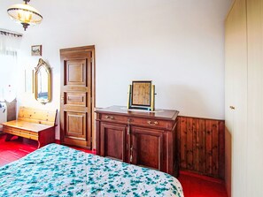 Ein Schlafzimmer mit einem Bett, einem Holzschrank, einer Bank und einem Spiegel.