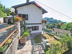 Ein zweistöckiges Haus mit Balkon, ein geparktes Auto davor und Blick auf die umliegenden Hügel.