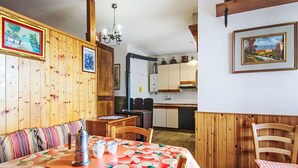 Un comedor con una mesa de madera, sillas y un banco. Hay cuadros en las paredes y una cocina al fondo.